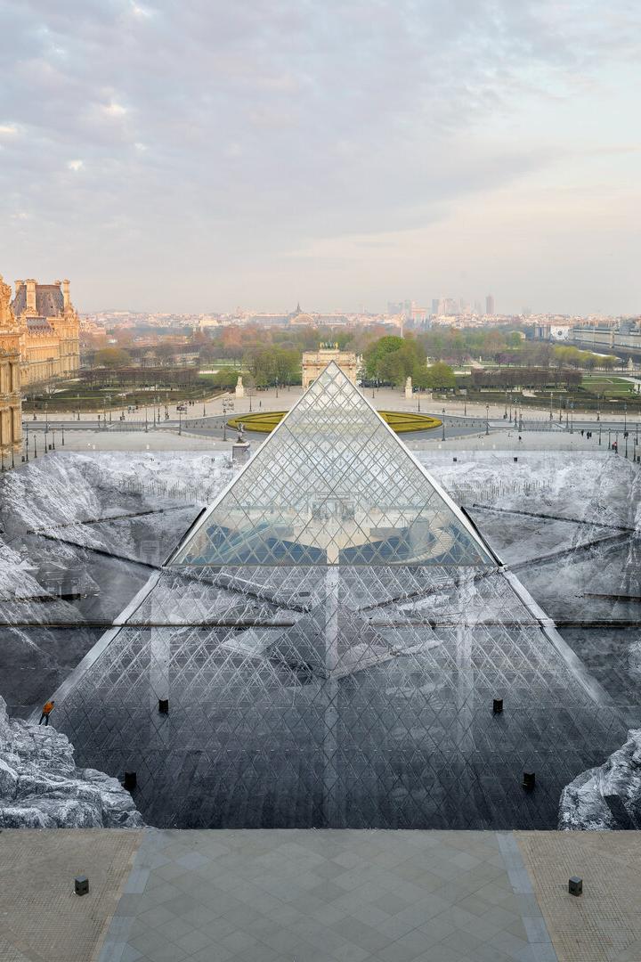 Die Glaspyramide des Louvre in Paris ist von einer großflächigen, schwarz-weißen Bodeninstallation umgeben, die eine felsige Landschaft darstellt.