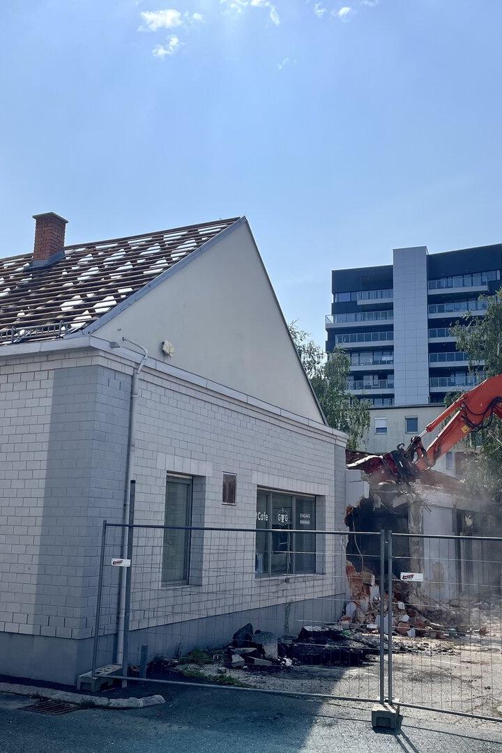 Bagger reißt ein Gebäude neben einem weißen Haus ab.
