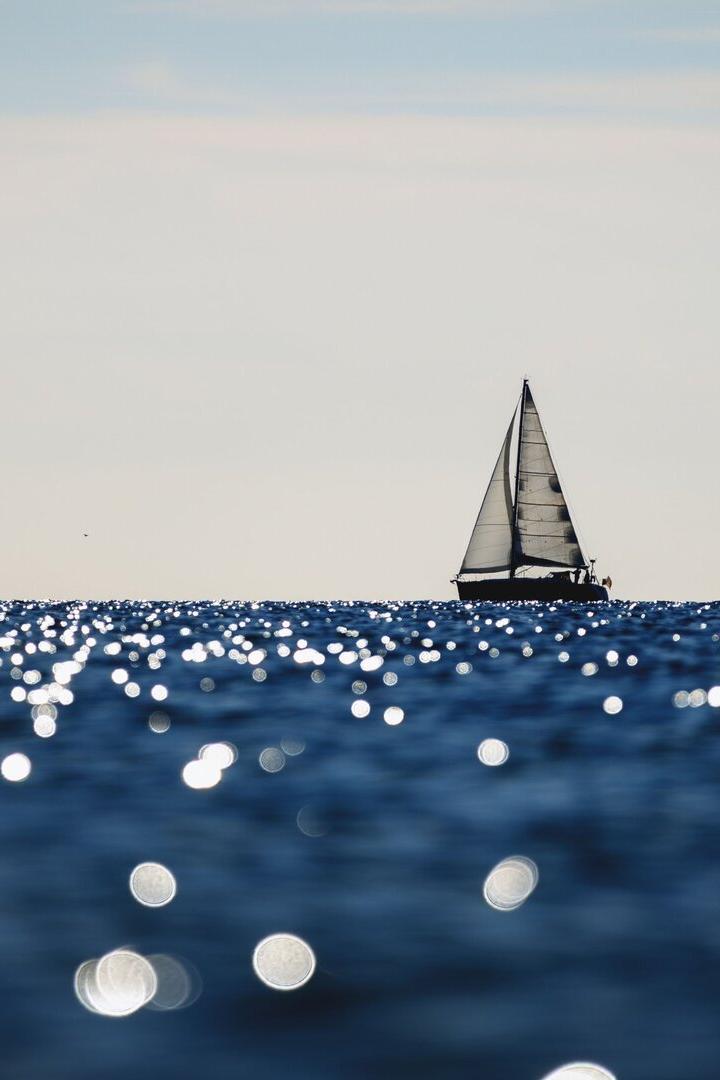 Segelboot auf glitzerndem Meer unter hellem Himmel.