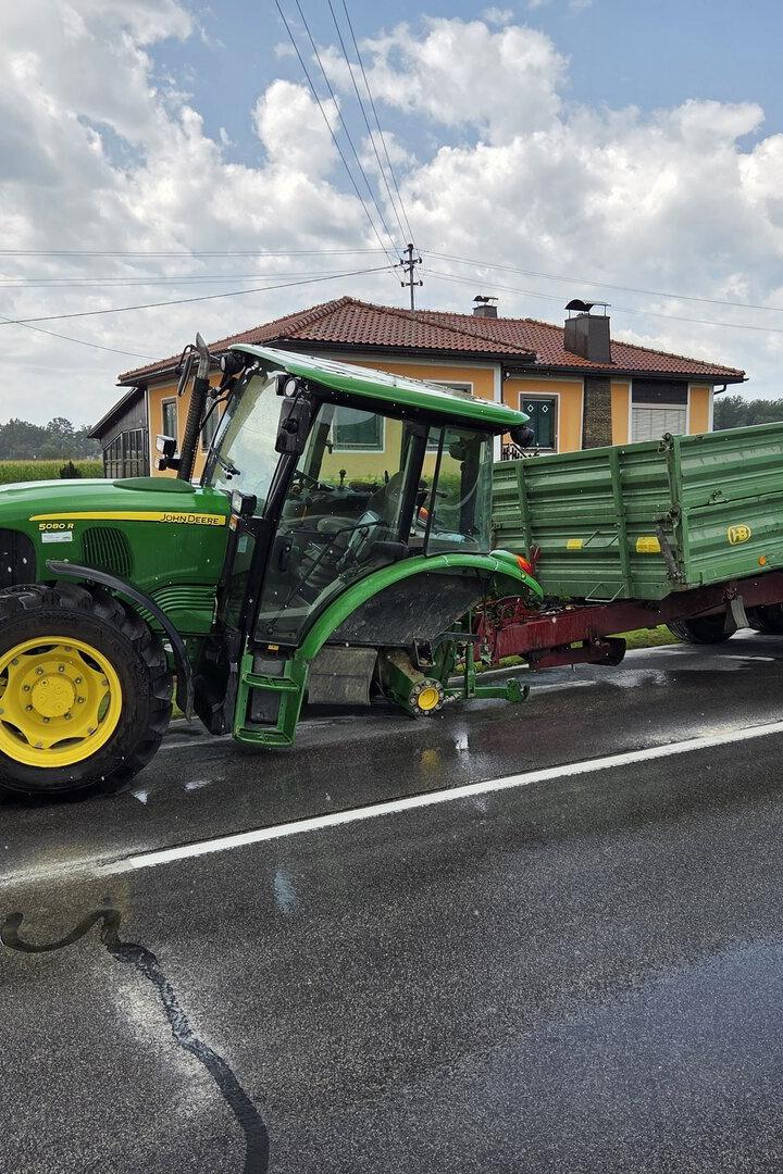 Grüner John-Deere-Traktor mit Anhänger steht auf nasser Straße vor einem Haus.