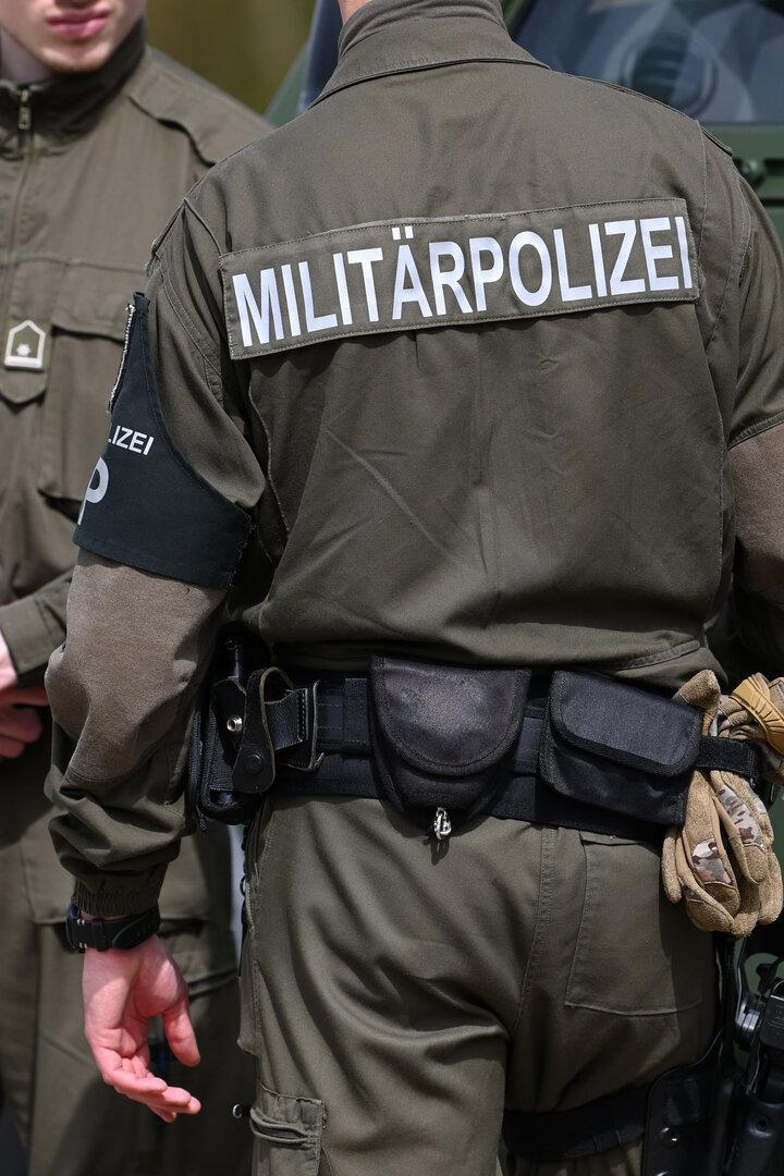 Zwei Militärpolizisten in Uniform stehen vor einem grünen Militärfahrzeug.