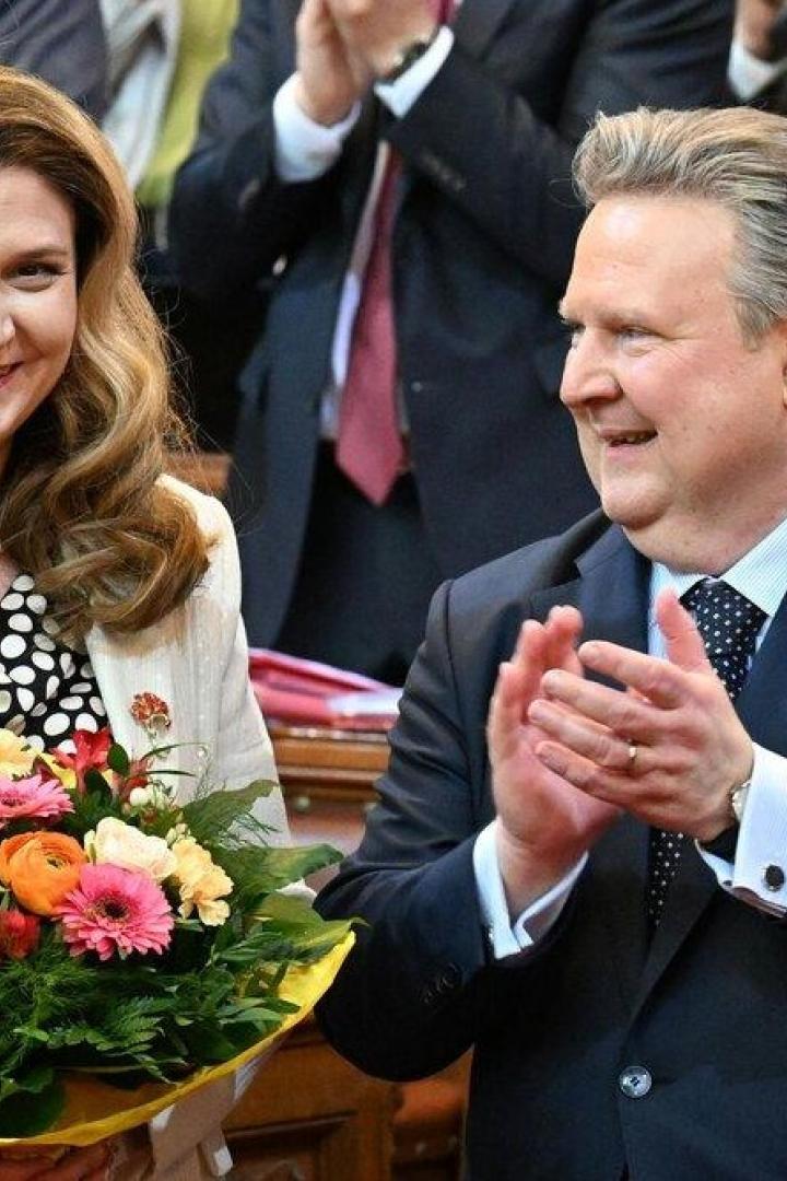 Eine Frau hält einen Blumenstrauß, daneben klatscht ein Mann im Anzug in einem feierlichen Saal.