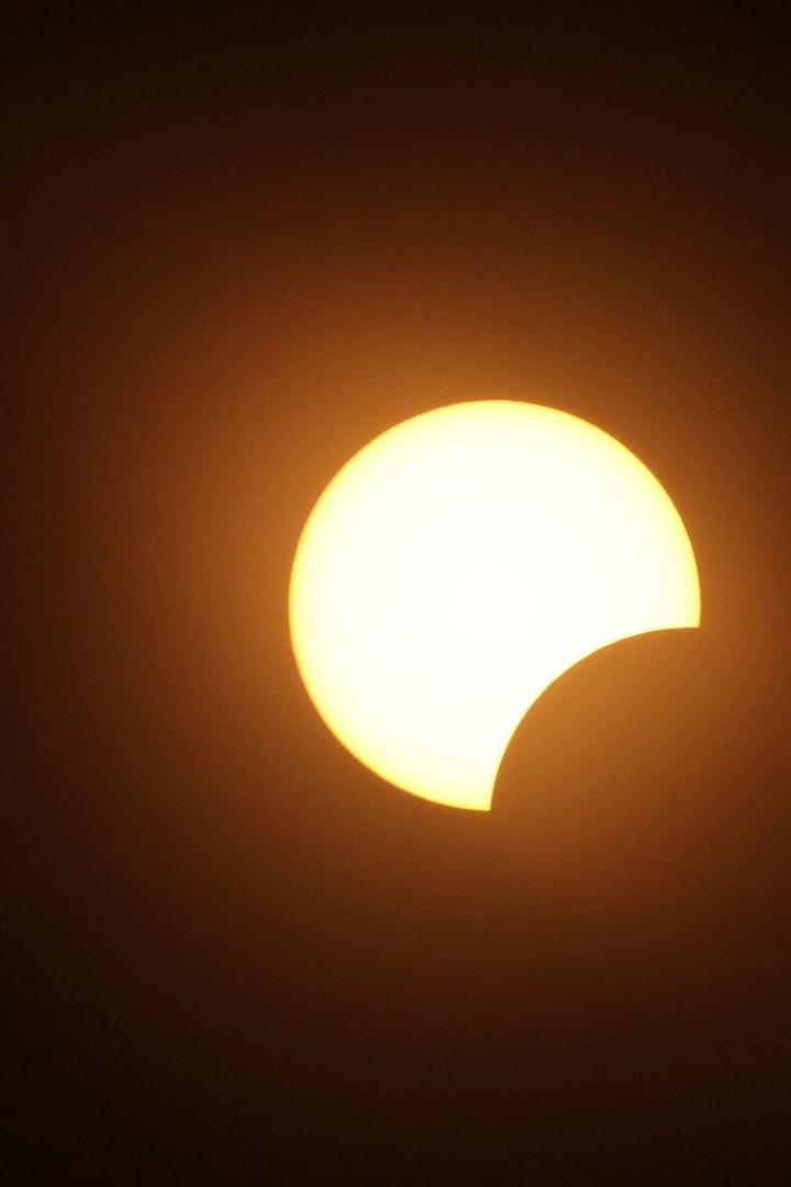 Teilweise verfinsterte Sonne mit dunkler Sichel vor orangefarbenem Himmel.