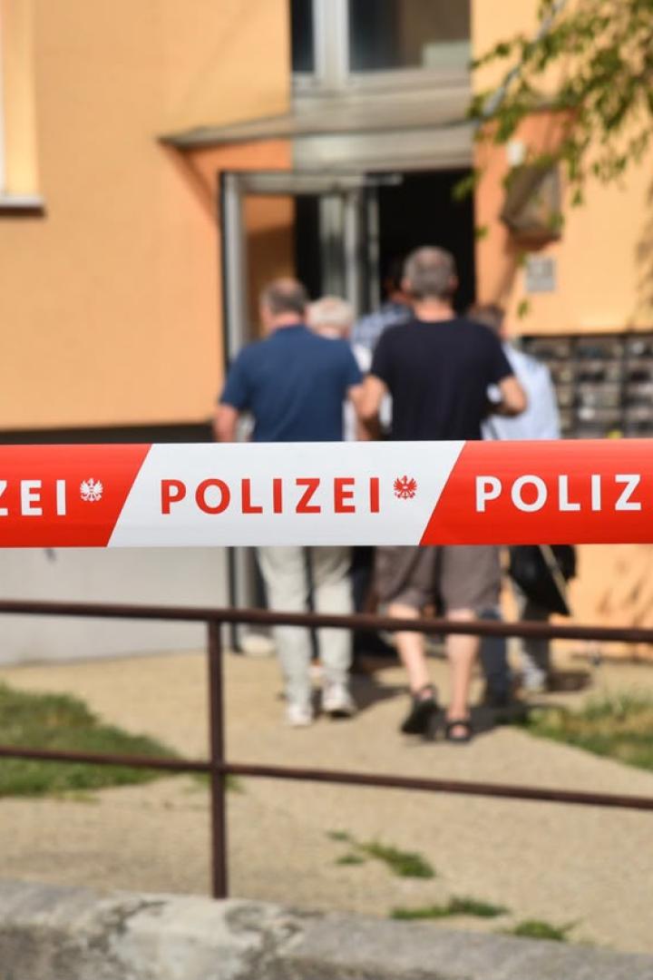 Polizeisperre vor einem Wohnhaus, dahinter gehen Menschen zum Eingang.