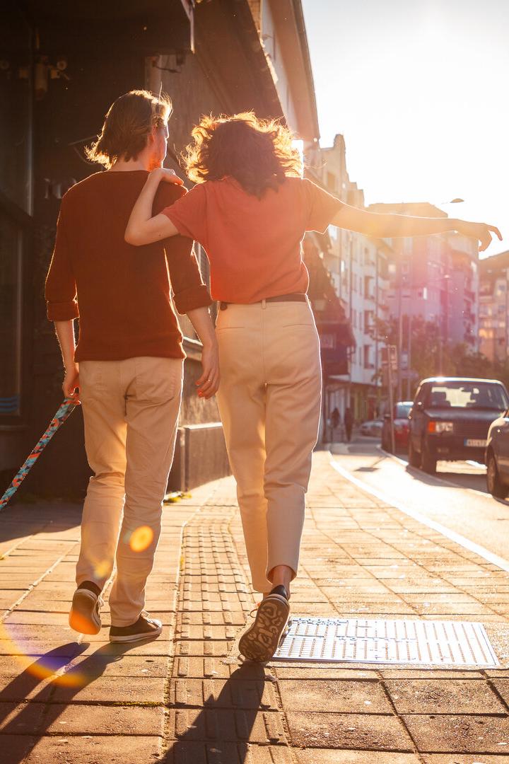 Back view of couple man and woman is walking around city with their dog. Sunset light in background