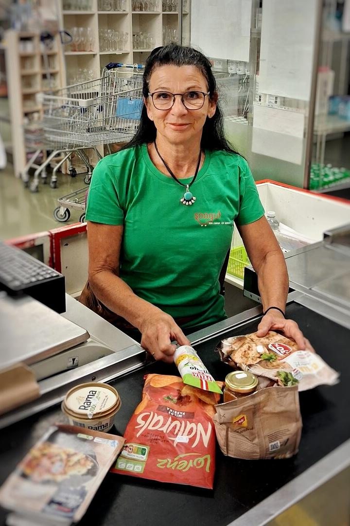 Frau an der Kasse eines Supermarkts mit mehreren Lebensmitteln vor ihr.