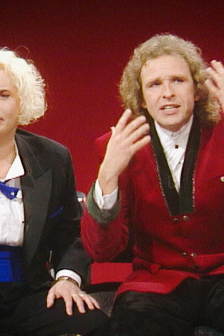 Hella von Sinnen und Thomas Gottschalk sitzen vor einem roten Hintergrund und unterhalten sich.