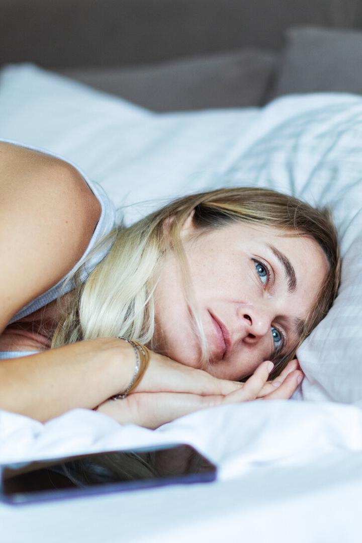 Mid adult woman lying in bed with mobile in depression