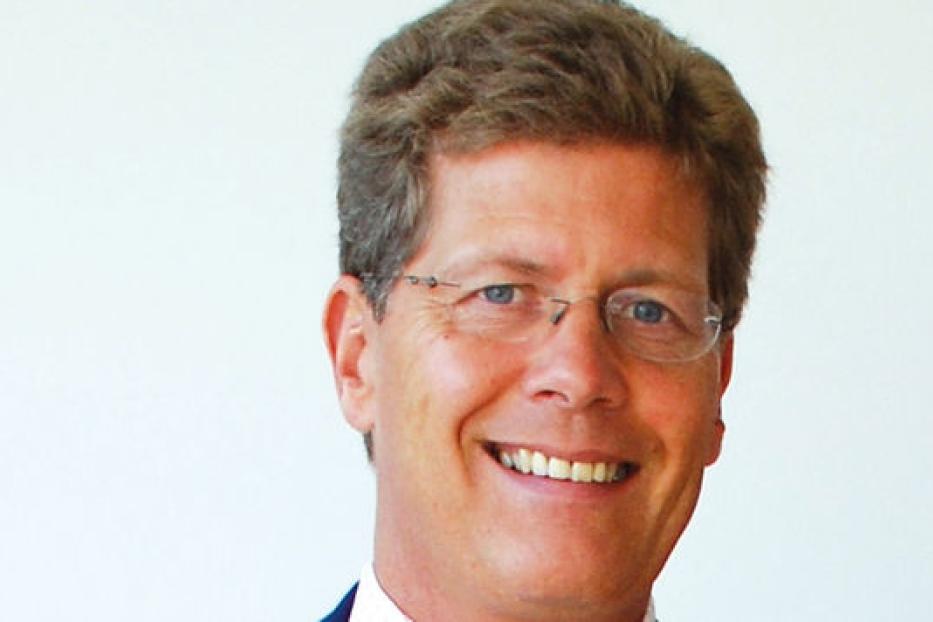 Ein lächelnder Mann mit Brille vor einem hellen Hintergrund.