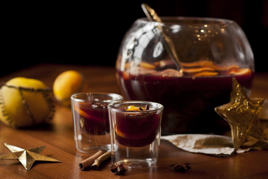 Zwei Gläser Glühwein stehen neben einer Schale mit Früchten und Gewürzen.