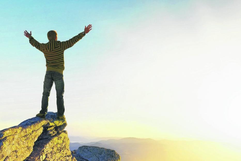 Ein Mann steht mit erhobenen Armen auf einem Felsen und blickt in die Ferne.