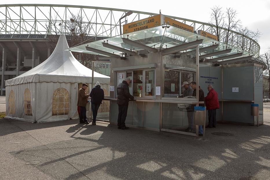 Vor dem Stadion stehen Menschen an einem Würstelstand an.