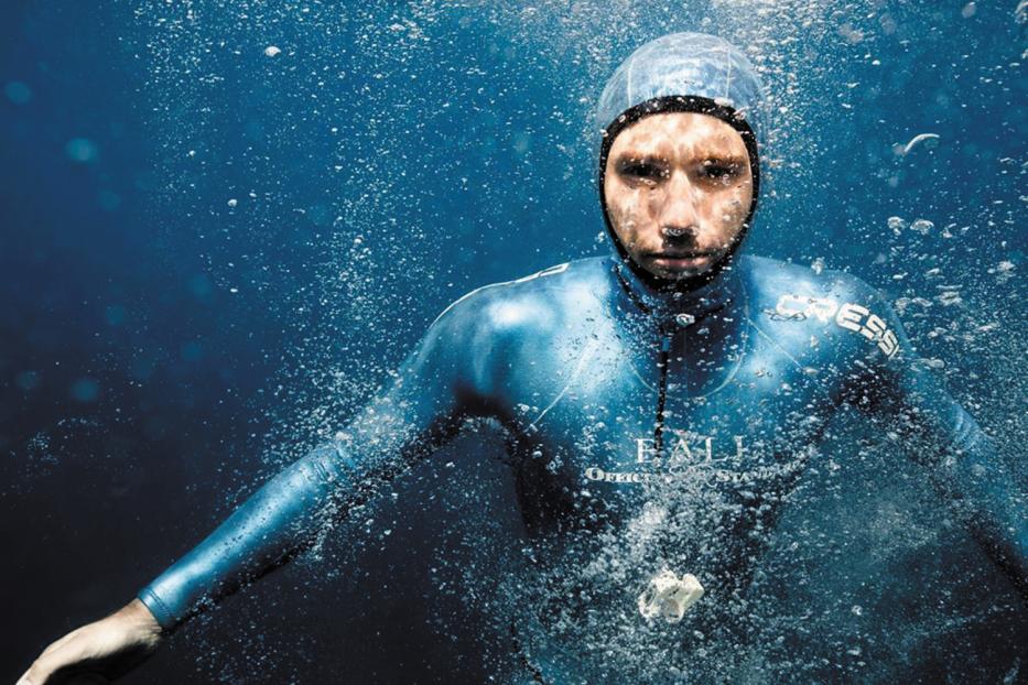 Ein Mann in einem blauen Neoprenanzug taucht unter Wasser.