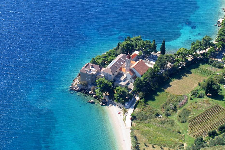 Luftaufnahme eines Klosters auf einer bewaldeten Halbinsel mit Strand.