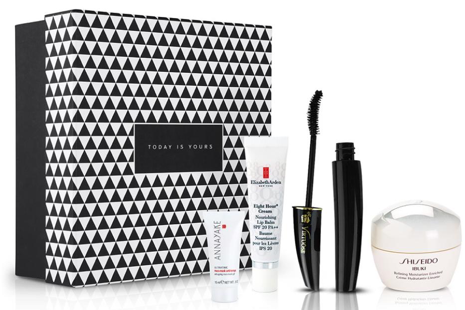 Ein Geschenkset mit Produkten von Elizabeth Arden, Shiseido und Annayake vor einer gemusterten Schachtel.