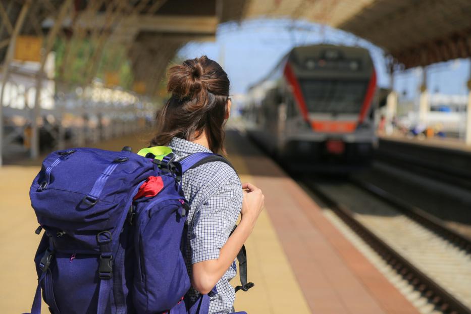 Eine Frau mit Rucksack wartet auf einem Bahnsteig auf den Zug.
