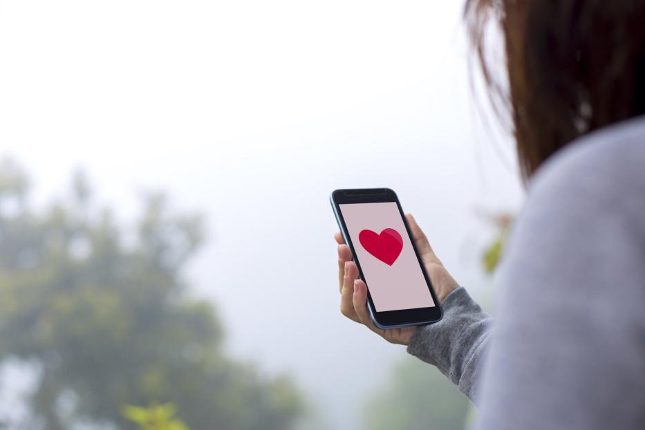 Eine Frau hält ein Smartphone mit einem roten Herzsymbol auf dem Bildschirm.
