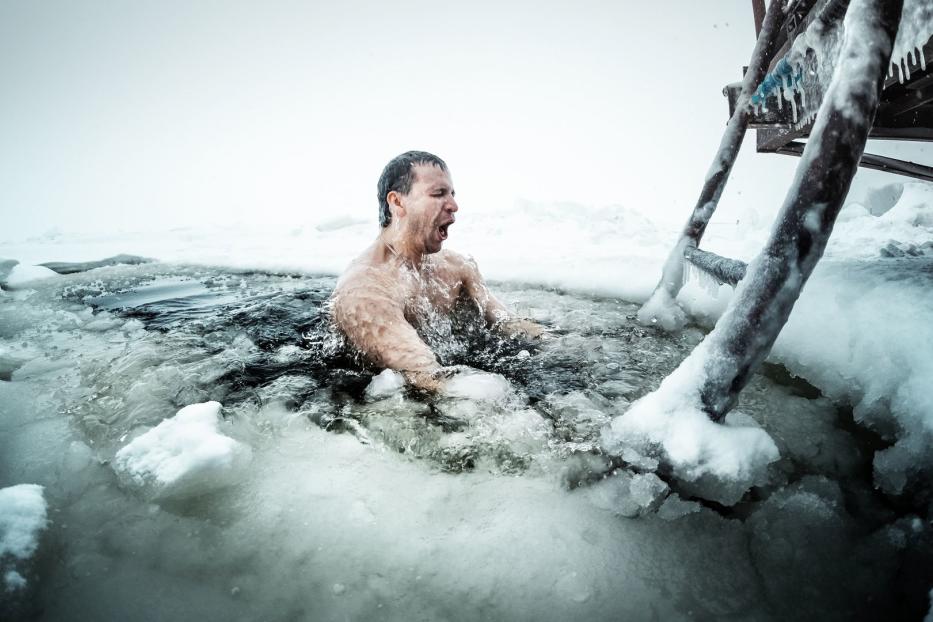 Ein Mann steigt in eiskaltes Wasser neben einer schneebedeckten Leiter.
