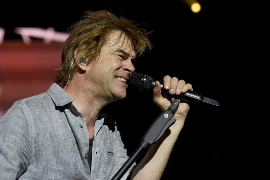 Ein Mann mit blonden Haaren singt in ein Mikrofon.
