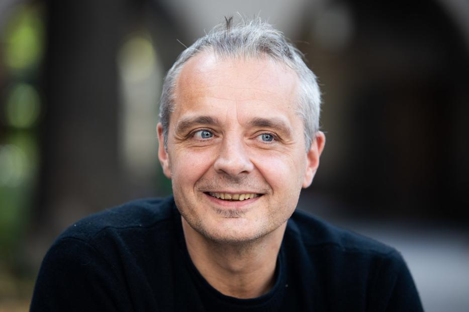 Ein lächelnder Mann mit grauen Haaren und blauen Augen blickt in die Kamera.