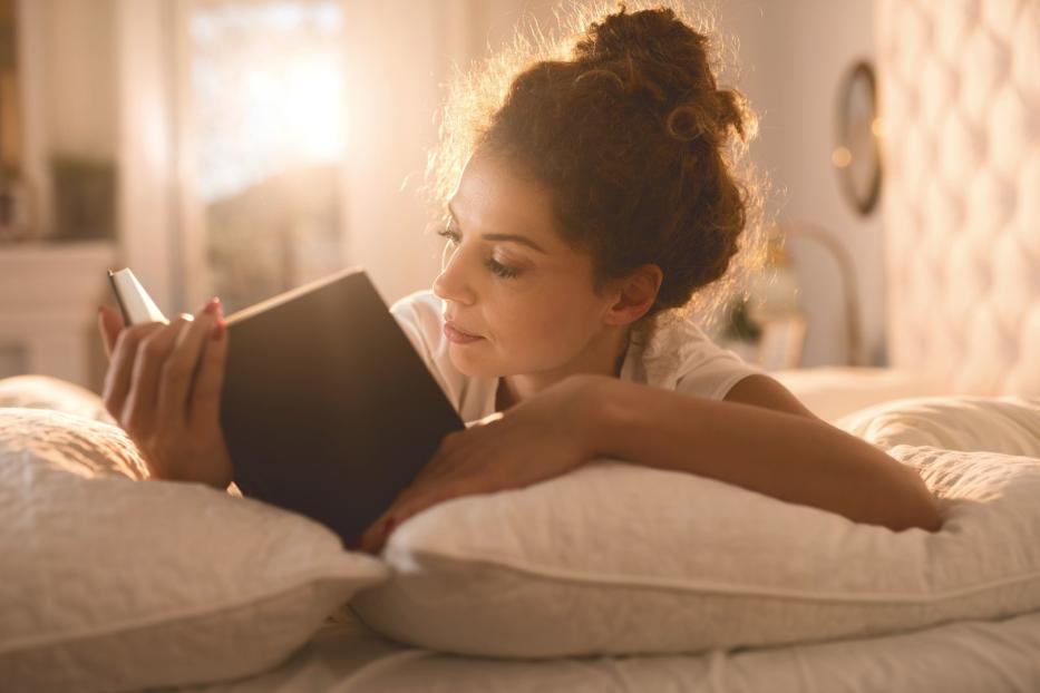 Eine Frau liegt im Bett und liest ein Buch.