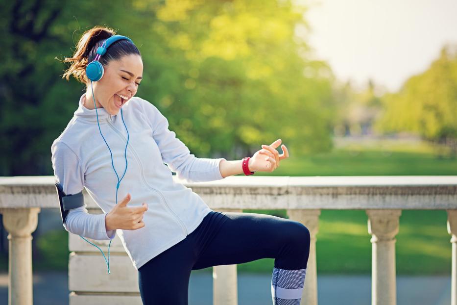 Eine sportliche Frau hört Musik und tanzt im Park.