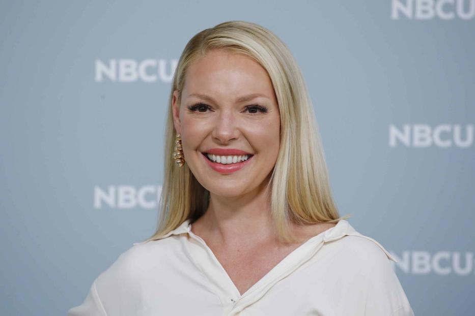 Katherine Heigl lächelt vor einem Hintergrund mit dem NBCU-Logo.