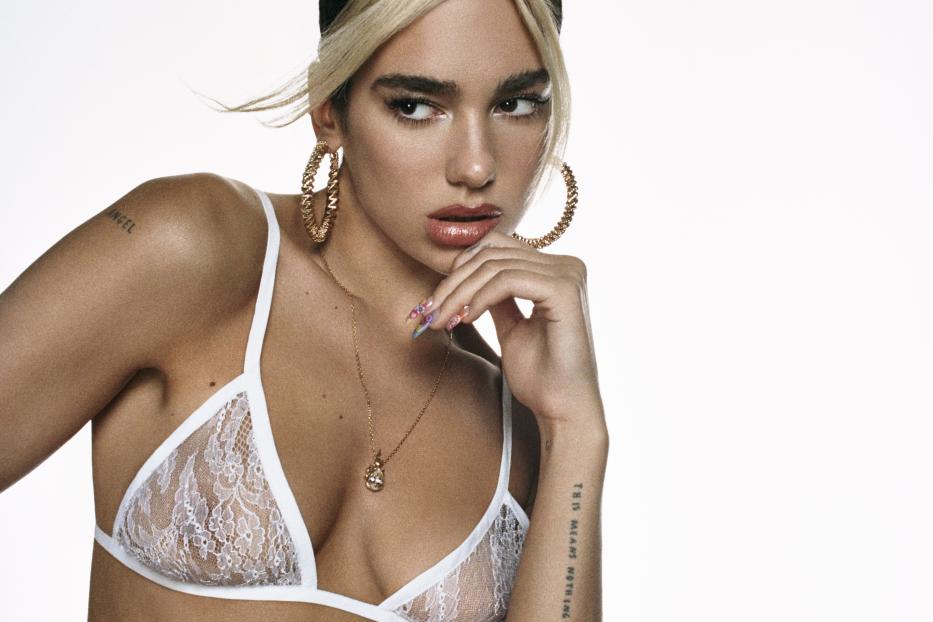 Dua Lipa posiert in einem weißen Spitzen-BH und einem roten Lederrock.