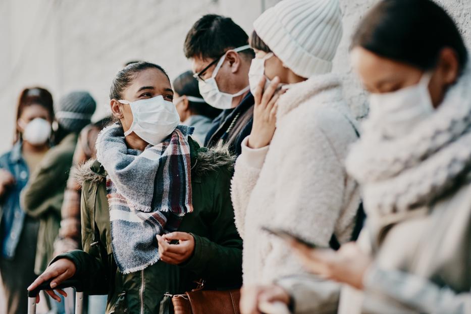 Eine Schlange von Menschen mit Gesichtsmasken wartet vor einer Wand.