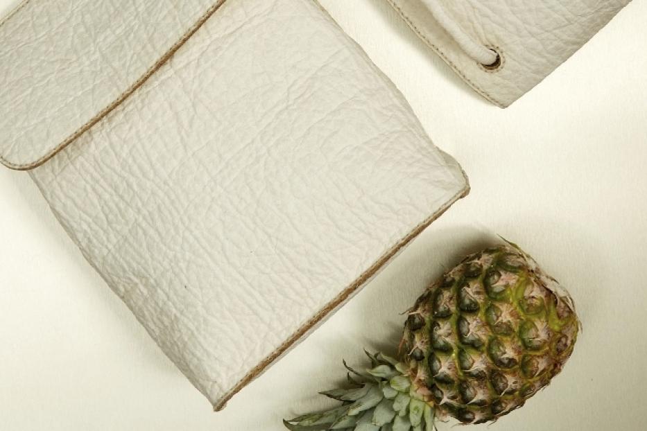 Eine Ananas liegt neben einer weißen Handtasche aus Ananasleder.