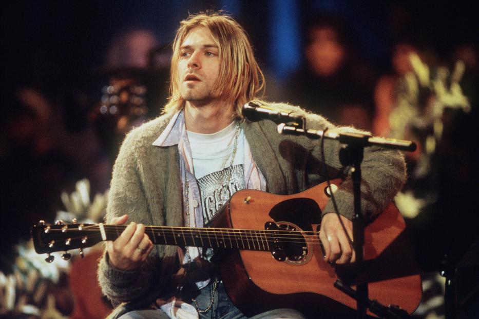 Kurt Cobain spielt auf der Bühne Akustikgitarre.
