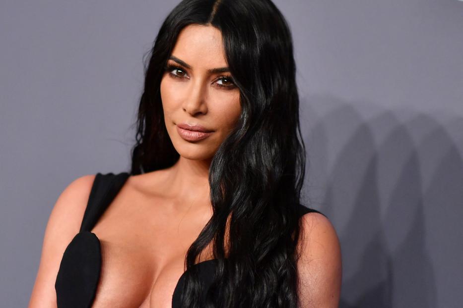 Kim Kardashian posiert in einem schwarzen Kleid vor einem grauen Hintergrund.