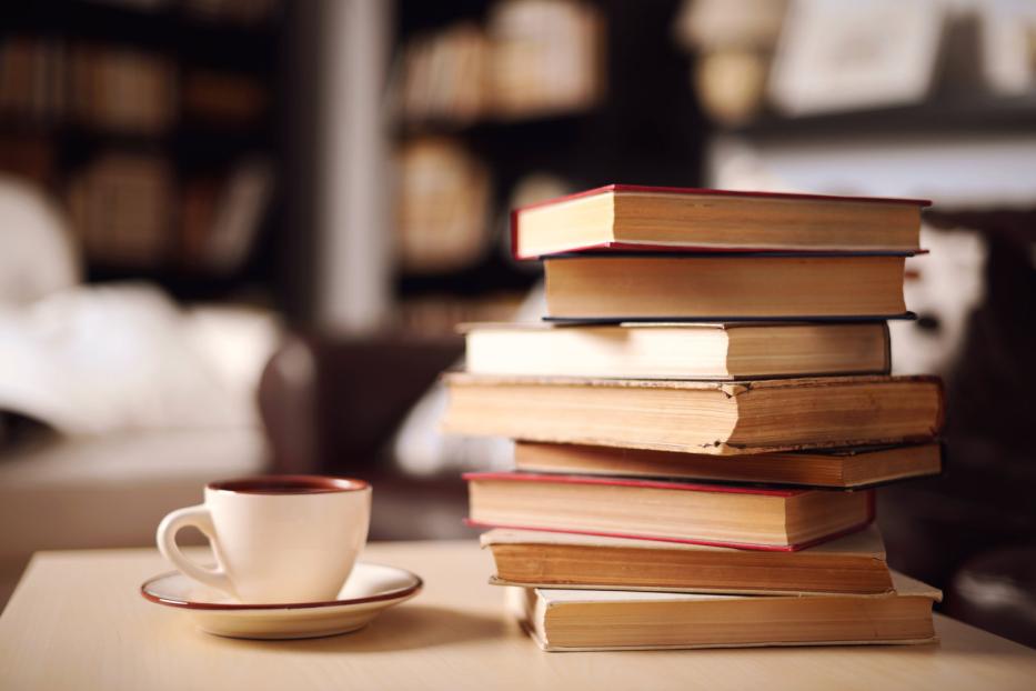 Eine Tasse Kaffee steht neben einem Stapel alter Bücher.