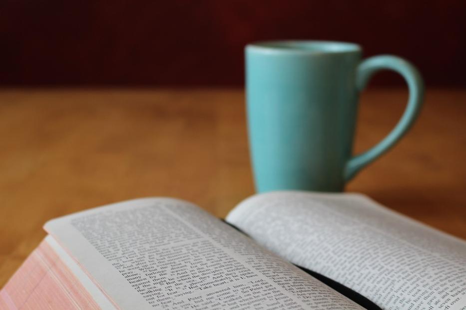Eine geöffnete Bibel liegt neben einer hellblauen Tasse.