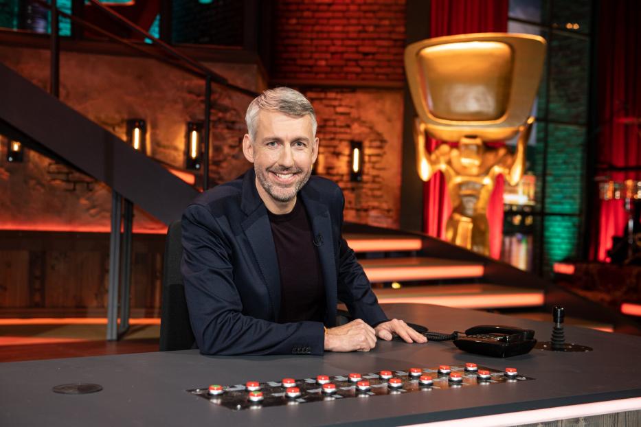 Ein Mann mit grauem Haar sitzt an einem Tisch mit vielen Knöpfen.