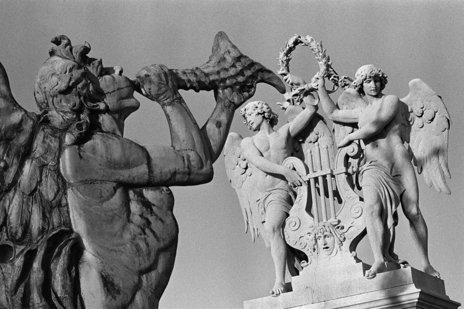 Detailaufnahme von drei Skulpturen mit geflügelten Figuren, von denen eine ein Horn bläst.