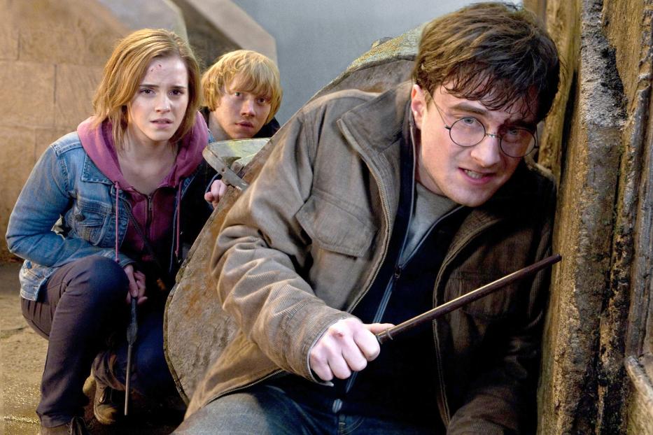 Harry Potter, Hermine Granger und Ron Weasley ducken sich mit gezückten Zauberstäben.