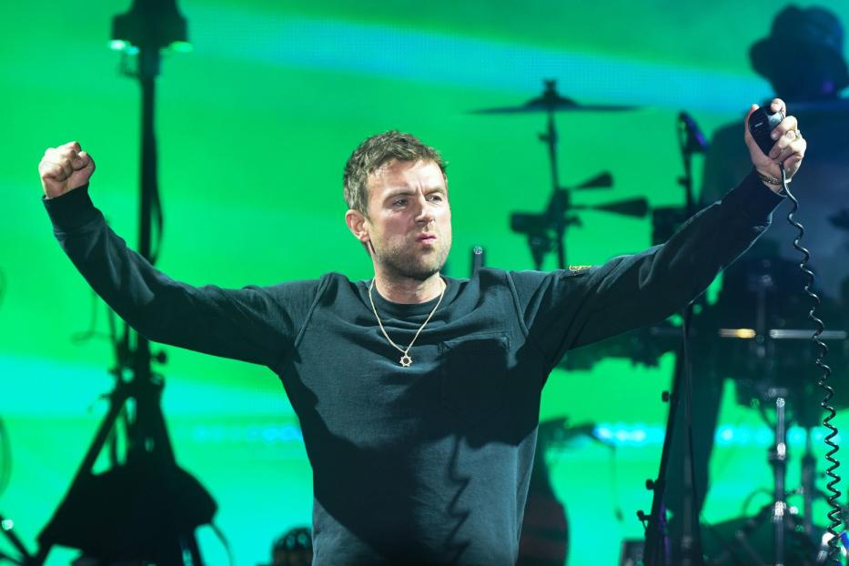 Damon Albarn von Blur tritt mit einem Mikrofon in der Hand auf einer Bühne auf.