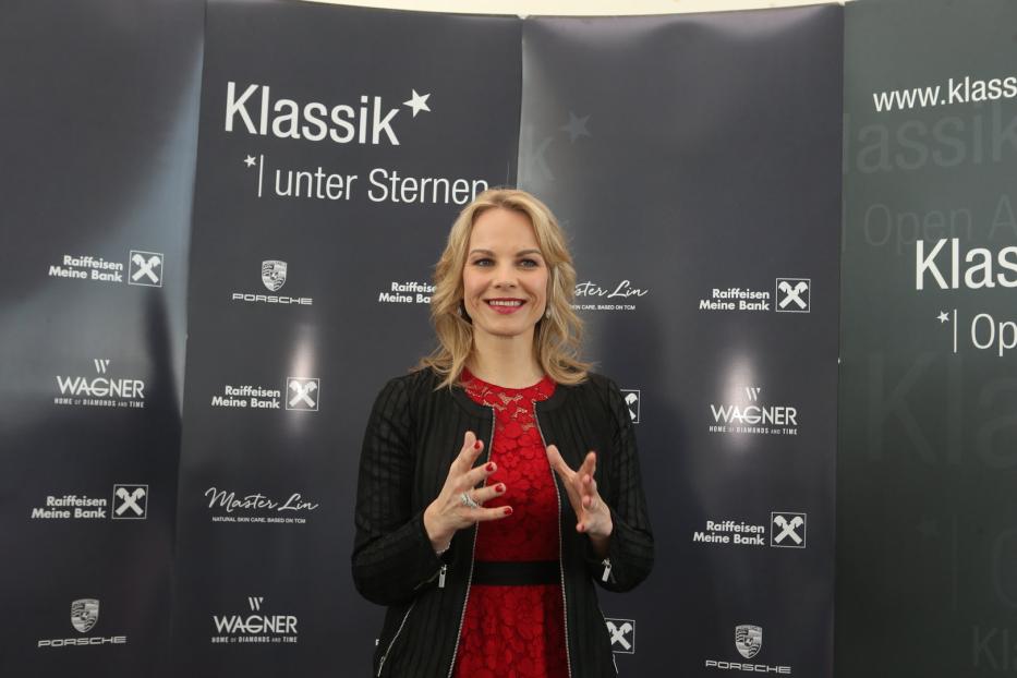 Eine Frau in einem roten Kleid posiert vor einem Banner für „Klassik unter Sternen“.