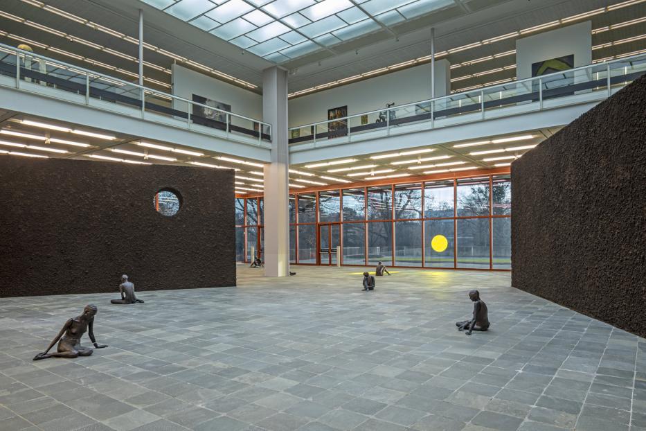 In einem Ausstellungsraum sitzen mehrere dunkle Statuen auf dem Boden.