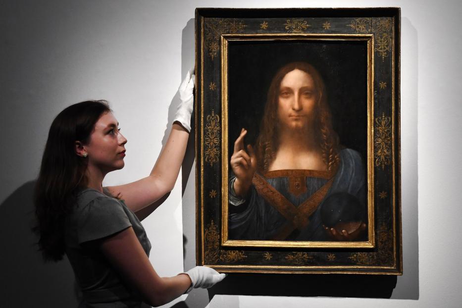 Eine Frau mit weißen Handschuhen hantiert mit dem Gemälde „Salvator Mundi“ von Leonardo da Vinci.