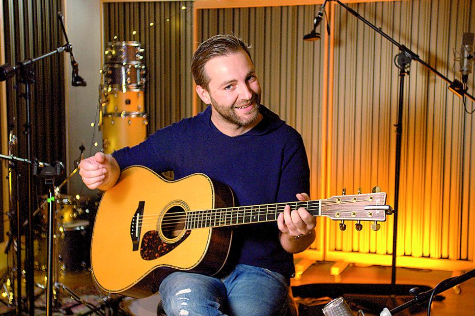 Ein Mann sitzt in einem Tonstudio und spielt Gitarre.