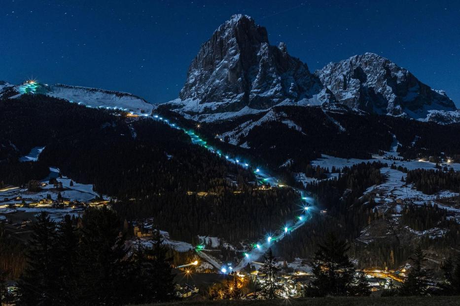 Eine Skipiste schlängelt sich nachts beleuchtet einen Berg hinab.