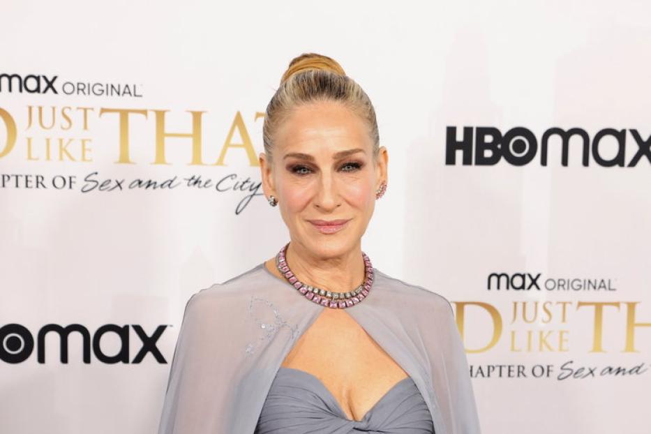 Sarah Jessica Parker in einem grauen Kleid mit rosa Akzenten auf einem roten Teppich.