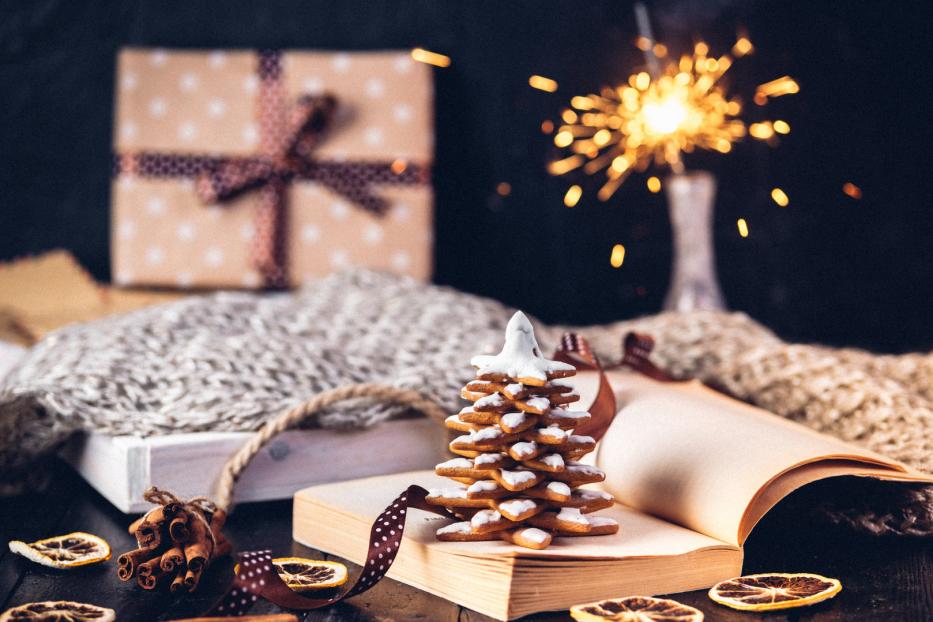 Ein Lebkuchen-Tannenbaum steht auf einem Buch, umgeben von weihnachtlicher Dekoration.