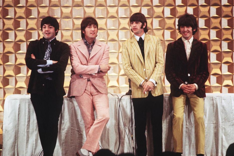 Die Beatles posieren in Anzügen vor einem gemusterten Hintergrund.