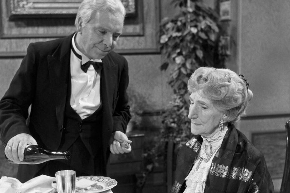 Ein Butler serviert einer älteren Dame ein Getränk.