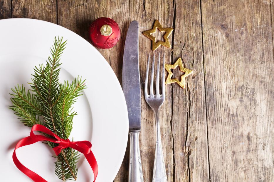 Ein festlicher Weihnachtstisch mit Tannenzweig, roter Kugel und goldenen Sternen.