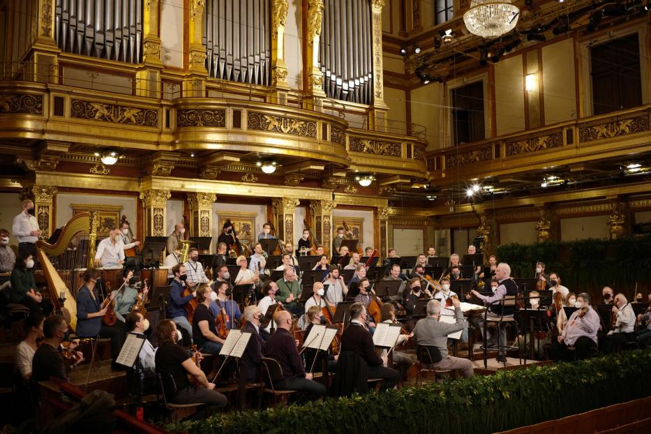 Ein Orchester spielt in einem opulenten Konzertsaal mit einer großen Orgel im Hintergrund.