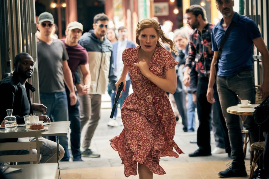 Jessica Chastain rennt in einem roten Kleid mit einer Waffe in der Hand durch eine Menschenmenge.